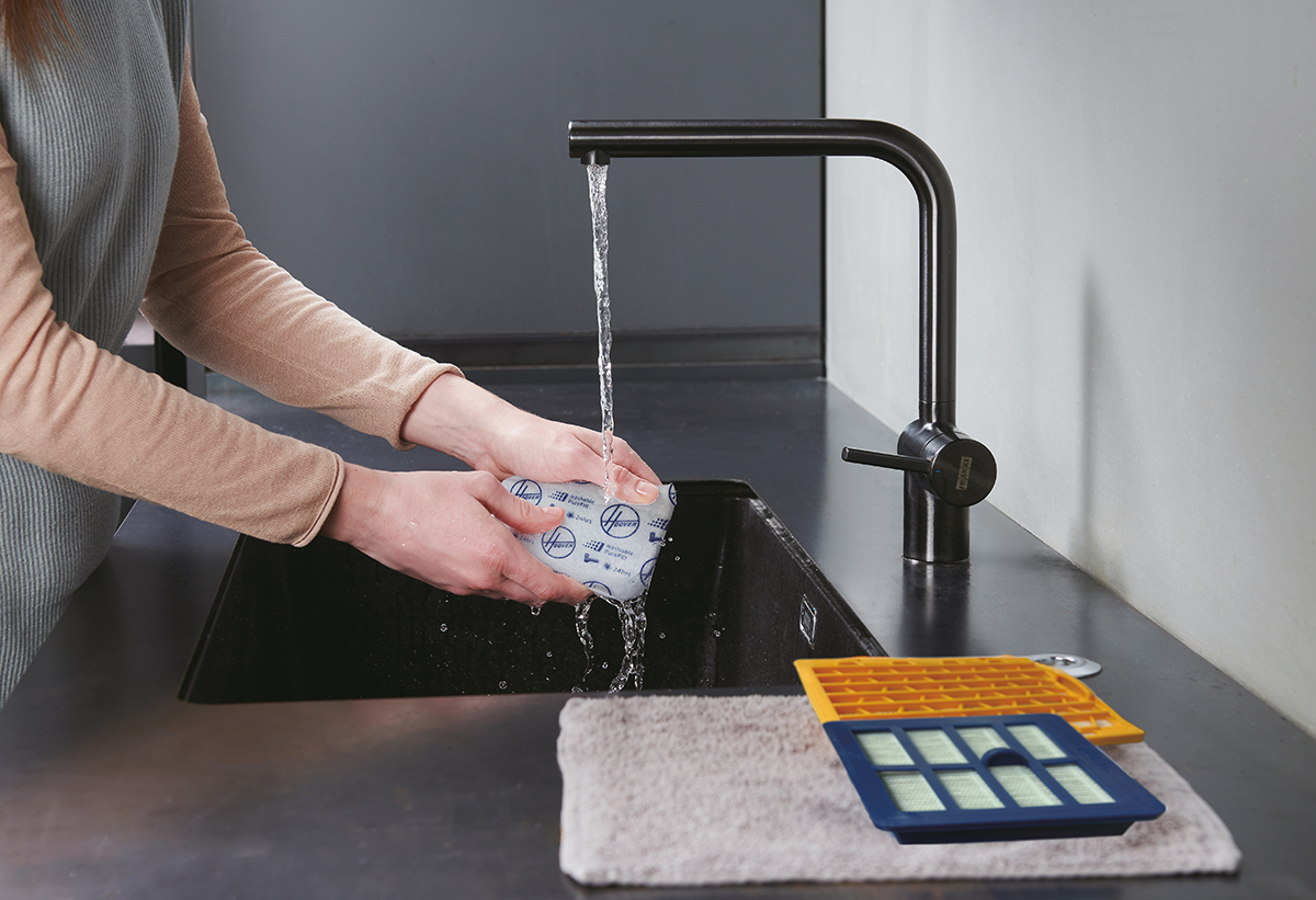 Μία γυναίκα πλένει το φίλτρο στην κουζίνα